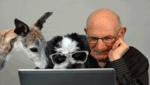 man looking at his laptop with two dogs looking at it with him