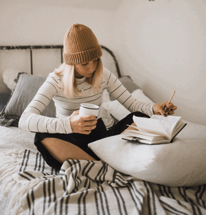 lady reviewing her writing while sitting on her bed with a coffee mug in one hand