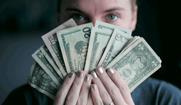 lady holding up several different American dollar bills, held fanned out in her hands, in front of her face